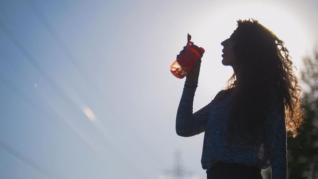 Cyclist pulls out of the backpack water and drinking background of the sun, sports in the Park, legs cyclist girl, bike on the grass, telephoto shot