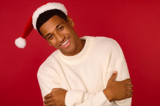 Christmas spirit. Young smiling guy in a white sweater and santa hat