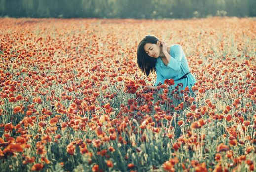 Beautiful girl walking in red poppy flower field in summer.