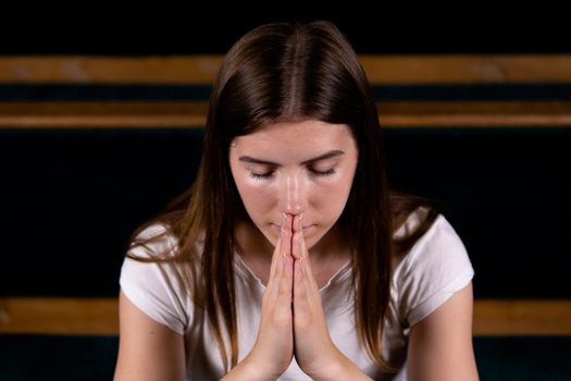 A Christian girl in white shirt is sitting and praying with humble heart in the church.