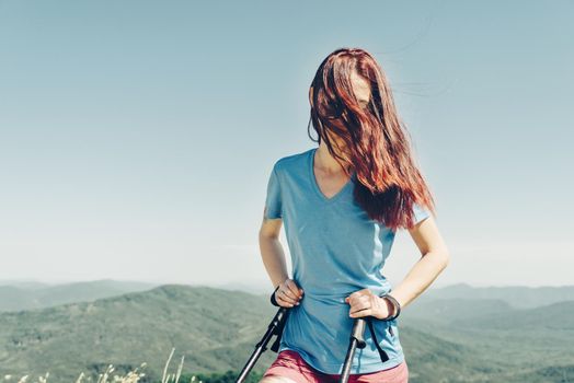 Sporty girl in a t-shirt and shorts walking with trekking poles high in summer mountains.