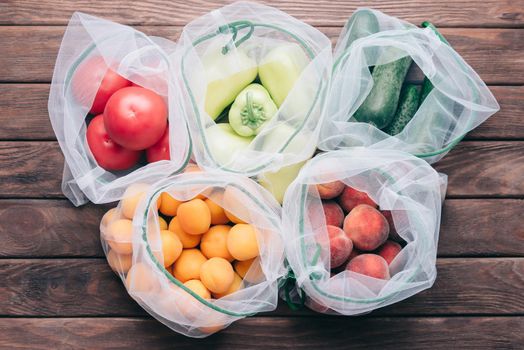 Fresh fruits and vegetables in reusable eco bags on a wooden background, top view. Zero waste and no plastic concept.