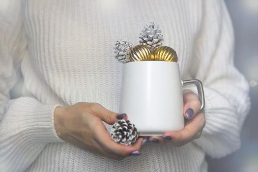 white christmas cup on woman hands with pine cones and golden balls -winter mug close up for new year time concept