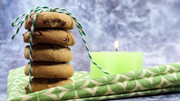 American chocolate chip cookies in a stack tied with thread on a green napkin and a candle. Traditional rounded crunchy dough with chocolate chips. Bakery. Delicious dessert, pastries