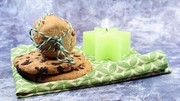 American chocolate chip cookies in a stack tied with thread on a green napkin and a candle. Traditional rounded crunchy dough with chocolate chips. Bakery. Delicious dessert, pastries