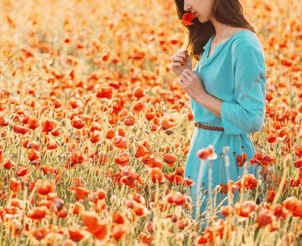 Smiling young woman smelling a red poppy in flower meadow on summer nature.