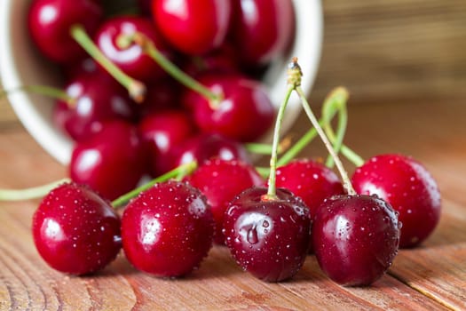 Cherries on wooden table with water drops in the ceramic cup. Closeup. Selective focus