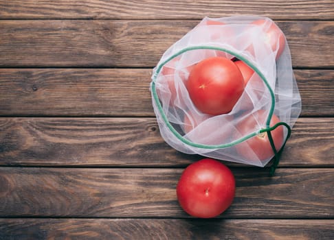 Reusable eco bag with fresh tomatoes on a wooden background. Zero waste concept. Copy-space in left part of image.