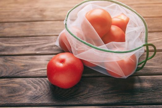 Reusable eco mesh bag with tomatoes on a wooden background. Zero waste concept.