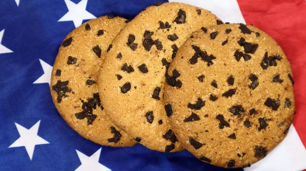 Patriotic cookies. Three rounded traditional chocolate chip cookies on the background of the flag of the United States of America. Delicious sweet pastries, dessert. America's favorite treat