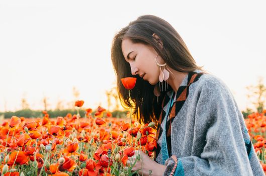 Dreamy attractive brunette young woman smelling a red poppy in flower meadow, summer vacations.
