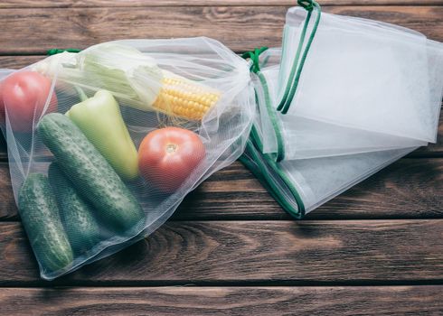 Fresh vegetables in reusable eco bag near empty mesh package on a wooden background, top view. Zero waste and no plastic concept.