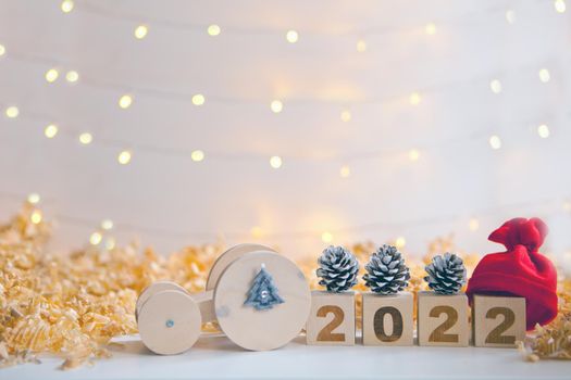 wooden car driving new year numbers 2022, red hat and pine cones. toy car carrying timber blocks. Happy new year celebration and Christmas approach. Lights and copy space