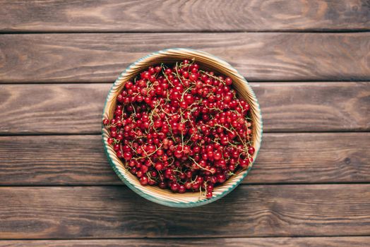 Fresh ripe red currant in a bowl on a wooden background, top view.