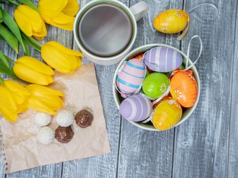Top view of Easter eggs and a cup of tea. Tulips live on a light wooden table