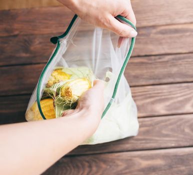 Female hands putting fresh corn cob in reusable eco mesh bag. Zero waste and no plastic concept.