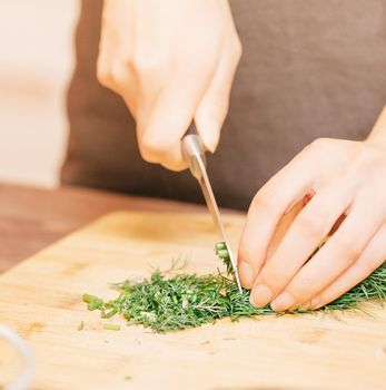 Close-up of female hands cutting greenery on wooden board in the kitchen.