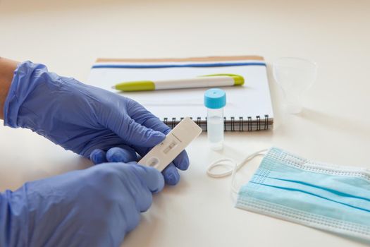 sars covid antigen test. mask and labglass at the table. doctor hands in blue gloves holding rapid test note with results