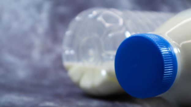 A half-empty and full plastic bottle of fresh regular milk lies on a dark gray marble or concrete backdrop. Close-up front view. World milk day concept. Nutrient fluid. Copy space.