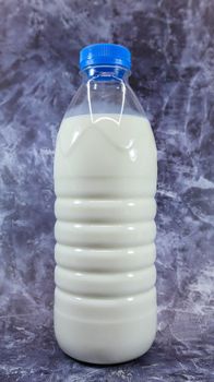 A plastic bottle of fresh regular milk on a dark gray marbled or concrete background. Close-up front view. World milk day concept. Nutrient fluid. Vertical photography