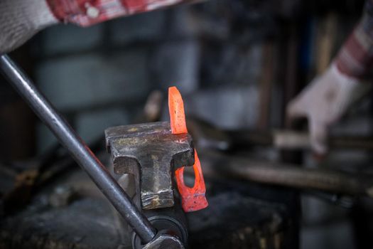 Workspace of blacksmith. Blacksmith working with red hot metal workpiece of new hammer in the vise. Telephoto shot