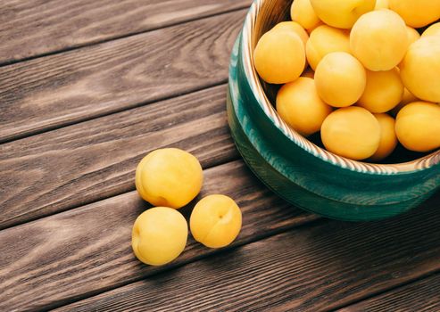 Fresh ripe yellow apricots in a bowl on a wooden table.