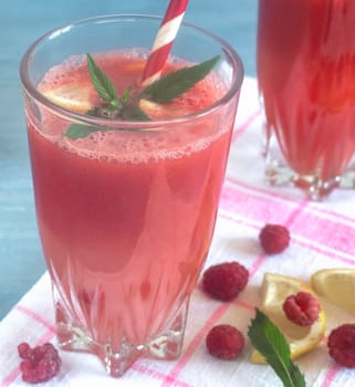 Fresh watermelon juice with raspberries and lemon in a glass. Slices of lemon and raspberries on the table. Front view. The concept of natural nutrition.