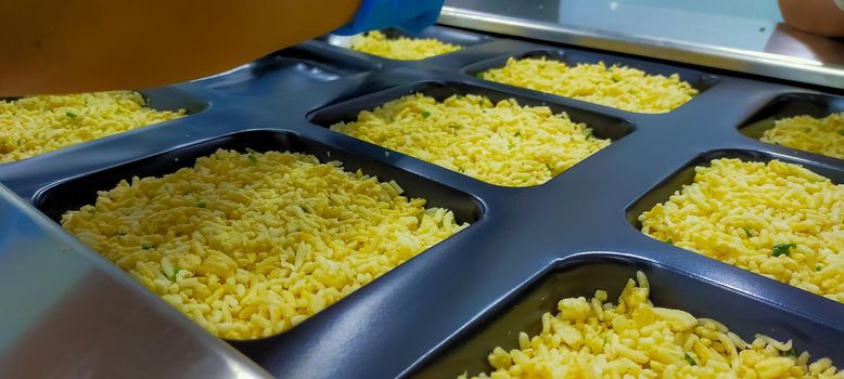 Frozen fried rice with egg in plastic tray waiting for top seal label with thermoforming machine in food factory. Frozen food industry. Ready meal process in manufacturing. Food packaging industry.