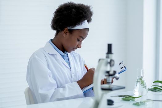 Young African American Scientist record analysis data and sit in room with other tools in laboratory and experiment with plant tissue science concept.