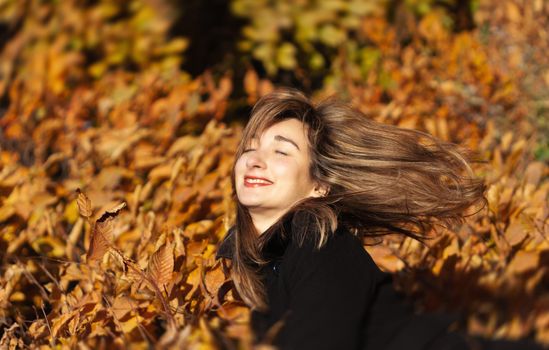 Smiling happy girl portrait with autumn leaves. Young woman among golden autumn leaves. Romantic moment in warm light. Park with yellow leaves and autumn atmosphere.