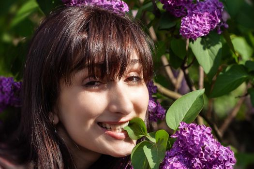 Portrait of a young beautiful woman posing among blooming lilacs. Woman among blossoming lilac bushes in spring.
