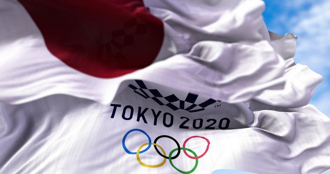 Tokyo, Japan, July 2021: Tokyo 2020 olympic flag waving with the Japanese flag blurred in the foreground. Selective focus. Tokyo 2020 olympics games were postponed to 2021 due to the covid-19 pandemic