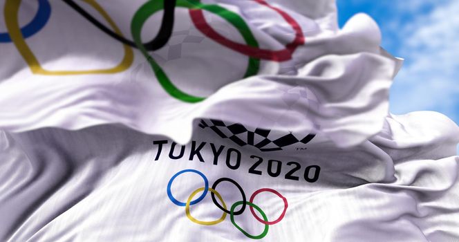 Tokyo, Japan, July 2021: Tokyo 2020 olympic flag waving with the Olympic flag blurred in the foreground. Selective focus. Tokyo 2020 olympics games were postponed to 2021 due to the covid-19 pandemic