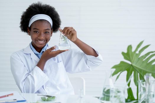 African American show flask that contain piece of plant tissue inside and smile with look to camera in laboratory or classroom.