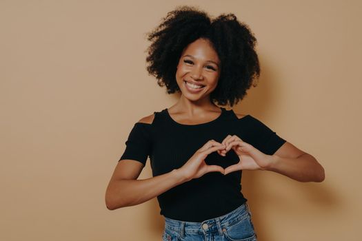 African american woman wearing casual clothes showing love gesture with heart shaped fingers, expressing healthy and marriage symbol with hands. Positive emotions and body language
