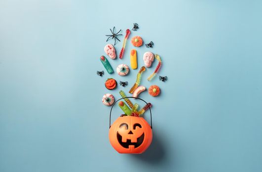 Halloween concept. Various halloween sweets in a pumpkin pot top view on blue solid background. Halloween party greeting card mock up