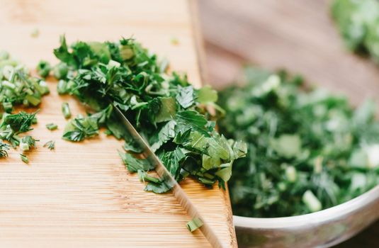 Sliced parsley greenery putting from wooden board into a plate, close-up.