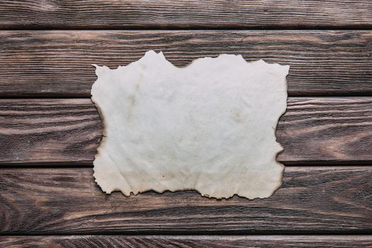 Old blank paper with burned edges on wooden background, top view. Free space for text.