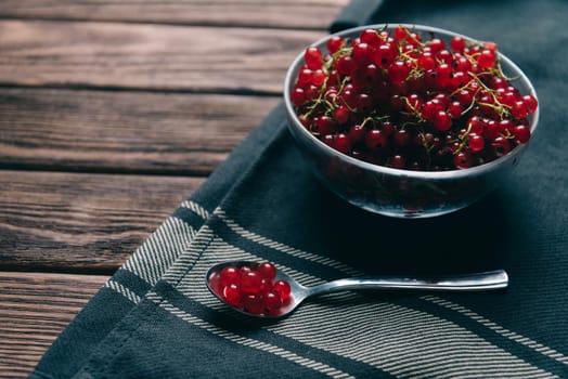 Fresh red currant in a bowl and spoon on rustic wooden background.