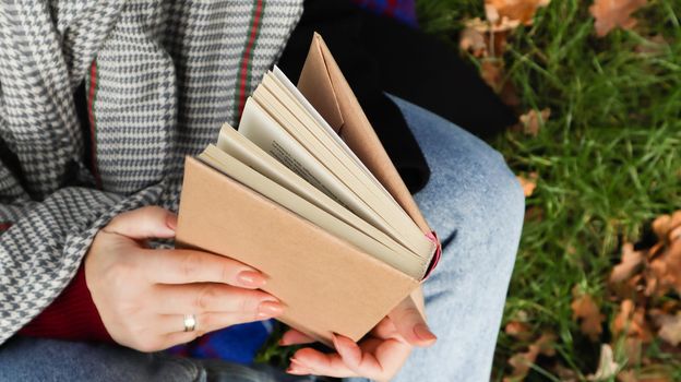 Girl reading a book in the autumn park. Female hands open the pages of a paper book outdoors on a warm sunny day. The student is preparing for the exam. Literary leisure in nature