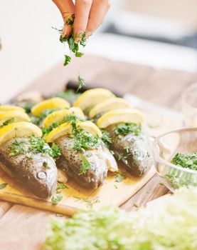 Chef woman putting greenery on dish of fish with lemons.