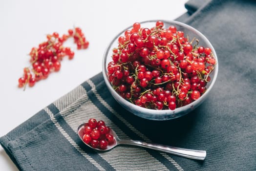 Fresh red currant in a bowl and spoon on textile napkin.