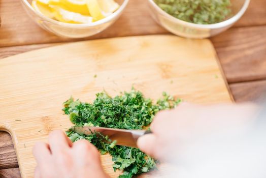 Woman cutting greenery food ingredient on wooden board, point of view.