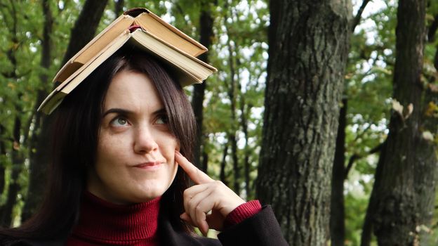 Portrait of a young and funny brunette in the park holding an open book on her head. Learning is fun. Woman balancing with books on her head. The student is tired of reading