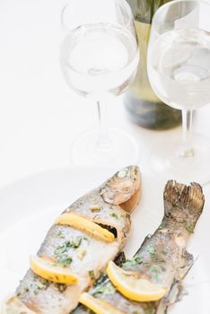 Seafood fish dish with lemons and greenery and two glasses of white wine for couple, romantic dinner.
