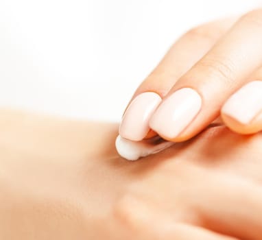 Close-up of young female hands with manicure of beige natural color applying moisturizing cream.