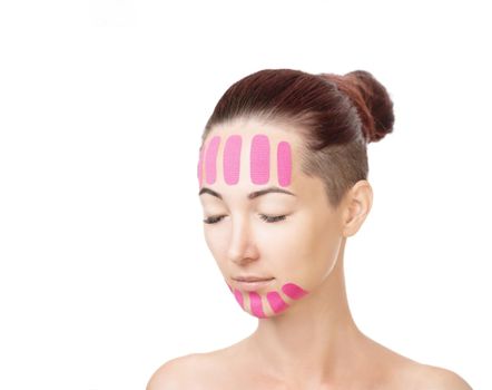 Beautiful young woman with vertical kinesio tapes on her forehead and chin for facelift, beauty procedure. Copy-space in left part of image.