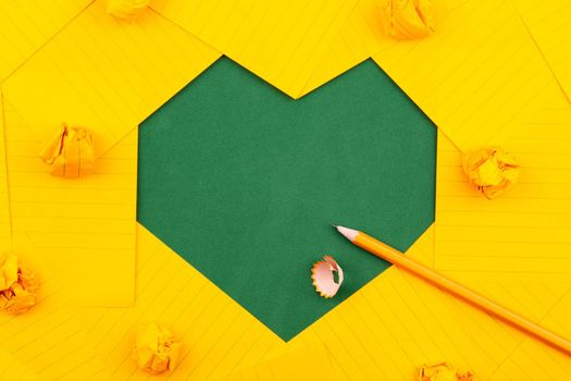 orange sheets of paper, pencil and crumpled papers lie on a green school board and form a frame heart shape
