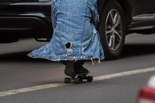 Man rides a skateboard sitting on a dividing strip on a city street, TELEPHOTO SHOT