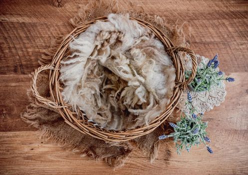 Cute cozy background for newborn photosession with flowers. Digital composite with basket filled with beige fur and standing on sackcloth. Provance style studio